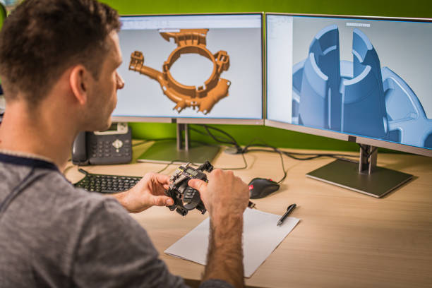 Engineer holding a machine part while making a 3D model on the computer.